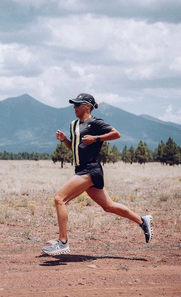 Male endurance runner in full stride running on a dirt road with mountains in the background. Enerza fuels distance runners.